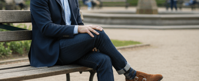 best shoes without lace. A casually dressed man stands against a warm-toned wall, wearing brown leather slip-on loafers with a minimalist design.